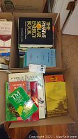 Two boxes filled with assorted books on various topics including sports, firearms, medical, and others. Books vary in size and cover design.
