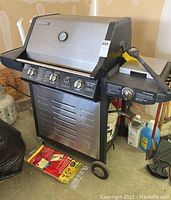 Front and side view of the Brinkmann propane grill with its control panel, thermometer on lid, and wheeled base for mobility.