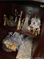 Shelf with brass candle holders, glass angel figurines, plastic bags with small ornaments, and assorted items.