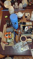 Photo of a collection of various vintage items including a thermos, teapot, glass jars, wooden shoe form, sad iron, and several small accessories on a table.