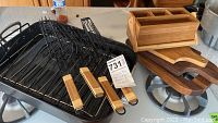 Black rectangular roasting pan with two metal roasting racks featuring wooden handles, alongside wooden kitchen items on a surface.