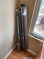 Two collapsible film screens with tripod stands leaning against the wall near a window in a corner of the room.