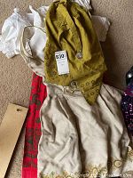 Two traditional German dresses laid out on carpet, one red and beige with mustard scarf, the other white with lace sleeves