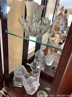 Top glass shelf showing large clear fluted-edge crystal bowl, porcelain figurine and vase edges