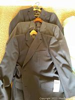 Three men's sport coats stacked on top of each other, visible in shades of gray and charcoal, showing typical sport coat features such as lapels and front pockets.