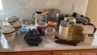 Wide view of lot on kitchen counter showing various items including cups, trivets, jars, and appliances.