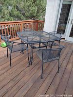 Overview of the entire patio dining set showing square metal mesh table with four chairs on a wood deck.