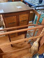 View of antique wooden cabinet with drawers and two vintage wooden racks in front, along with vintage straw broom leaning on the rack.