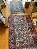 Large red and ivory geometric patterned rug laid on hardwood floor, smaller beige geometric rug seen in background