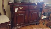 Front view of Thomasville wooden sideboard showing two drawers with brass handles and two cabinet doors with brass keyhole hardware.