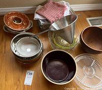 Photo showing wooden and glass bowls, round glass plate, metal mesh strainers, large conical metal strainer, and cloth towels.