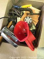 Box with various tools including red plastic funnel, paint strainer, hand saw, caulking gun, and wire brush