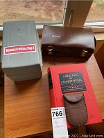 Image showing a gray Resusci Folding Bag II case, a brown leather Propper case, a red hardcover medical book titled 'A Practice of Anaesthesia,' and a small brown leather pouch.