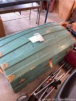 Full view of green vintage round top trunk with some wear and tear visible, showing rounded lid and metal corner protectors.