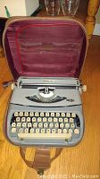 Open view of a vintage Royalite typewriter in its maroon fabric-lined case, showing the gray body and cream-colored keys.