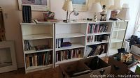 Four white Ikea MDF bookcases placed side by side, filled partially with books and items on top, showing overall appearance and size.