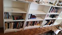 Photo of white bookshelves holding several books in various configurations, some stacked horizontally and some vertically.