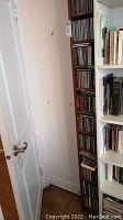 Photo showing tall wooden CD rack packed with CDs, located in corner next to bookshelf.