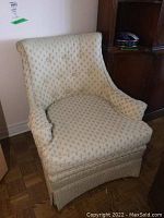 Two cream patterned upholstered arm chairs with tufted backs, rounded arms, removable seat cushions and pleated skirts.