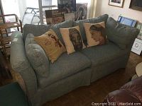 Two seater fabric couch with decorative throw pillows arranged on the couch, shown from front and angled side view.