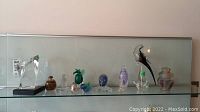 Wide view of glass art collection on glass shelf showing various animal figures, bottles and abstract forms.