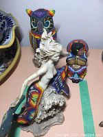 Front view of three Huichol beaded figurines on shelf.