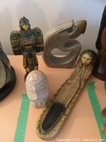 Four indigenous carvings on table: multicolored bird, beige female figure, white owl, grey bird head