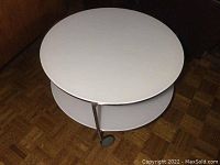 Full side view showing the white round two-tier table on three casters with chrome supports