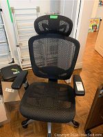 Front view showing black mesh seat, backrest, and curved adjustable headrest with black armrests and silver base on casters.