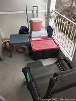 Patio area with multiple coolers, a small blue plastic table, various plant pots, and a black metal reclining lounge chair.