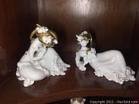 Front view of both white porcelain figurines with gold detailing displayed on a shelf