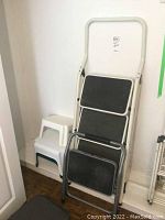 Full view of the folding metal stepladder, metal stepstool, and three stacked PVC stepstools against a wall.