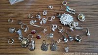 Wide view of assorted sterling silver jewelry items including rings, earrings, brooches on a wood grain surface