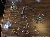 Overhead shot of enameled rabbit trinket box, folding lorgnette and scattered jewelry pieces on wood table