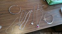 Full layout of seven sterling silver necklaces and chokers on wood surface.