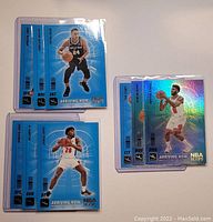 Nine Panini NBA Hoops Basketball Arriving Now 2020-21 cards. Three cards grouped on the right show a player in white jersey shooting. Four cards grouped on the top left show a player in a black jersey holding a basketball. Four cards grouped on bottom left show a player in a white jersey in defensive stance. All cards have holographic foil backgrounds and are individually sleeved in protective plastic.