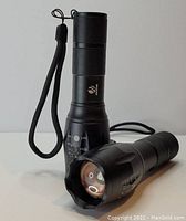 Two black tactical LED flashlights, one standing upright and one laying down to show frontal lens and side control panel.