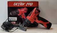 Photo showing a red and black Detlev Pro 12V cordless drill driver alongside its box, charger cable, and a set of drill bits.