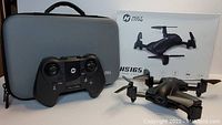 Photo showing Holy Stone HS165 drone with foldable arms and propellers, 2.4GHz remote controller, hard-shell gray carrying case, and original retail box.