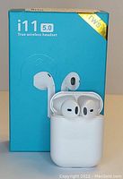 Photo of white i11 5.0 True Wireless Headset earbuds inside their white charging case, in front of the blue original box packaging.