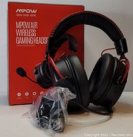 Mpow Air Wireless Gaming Headset placed in front of its original red and white packaging box. The headset is black with red accents, padded ear cups, adjustable headband, and attached microphone. Includes a plastic-wrapped accessory.