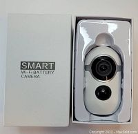 Photo of the white smart Wi-Fi battery camera in packaging with its retail box showing the product name.