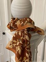 Brown silk scarf with a leaf motif draped on a white decorative post.