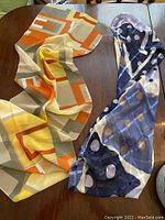 Photo shows two colorful scarves laid out on a wooden surface, one scarf with geometric patterns and the other with polka dots.
