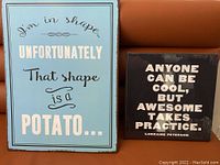 Two framed posters side by side on a brown couch, one black and one blue with humorous quotes.