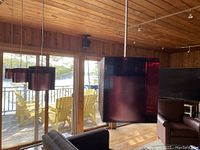 Four dark purple glass cube pendant lights hanging from ceiling steel wires in a living room setting with wooden ceiling and glass doors in background.