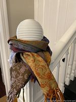 Scarf wrapped around a white spherical lamp showing the multicolor paisley pattern and fringed tassel ends.