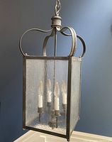 Front view of the black metal frame hanging lantern showing frosted glass panels and candle style bulbs inside.