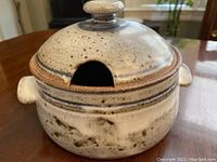 Stoneware crockery pot with lid on a wooden surface, showing side view with lid on, highlighting knob and thumb notch
