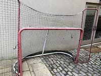 Photo of a used NHL sized hockey net with red metal frame and black netting, showing wear and rust.